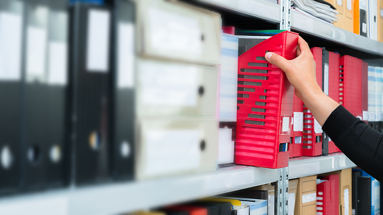 Mans hand picking a blank blind folder with files from the shelf. Archival, stacks of documents at the office or library