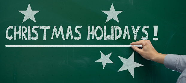 School background banner - Teacher at green school blackboard with chalk in his hand writes the text Christmas holidays and draws star symbols