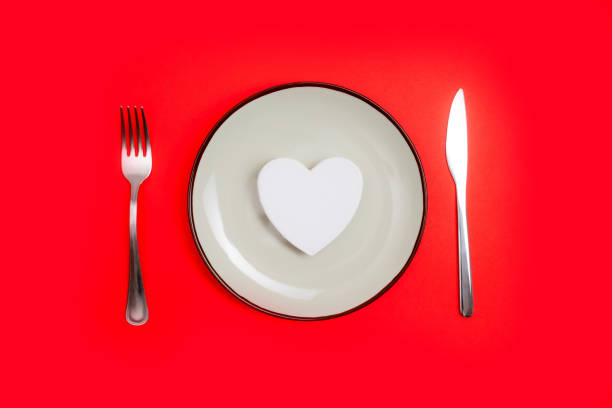 istock Romantic valentines day dinner idea concept. Heart on plate and silver wear on red background. 1443843737