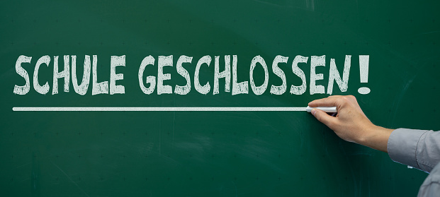 Green blackboard in the classroom with the inscription: SCHOOL CLOSED! with German text