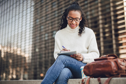 It's all easier when done digitally. A young black woman sits on a bench and writes down her daily obligations in her diary.