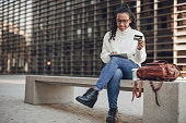 A young black woman is shopping online on a digital tablet while sitting on a bench on the boardwalk