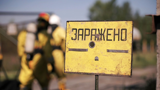 A sign warning of danger. Clip. People performing work in a dangerous area going to a gas mask on the background of a sign warning of danger.