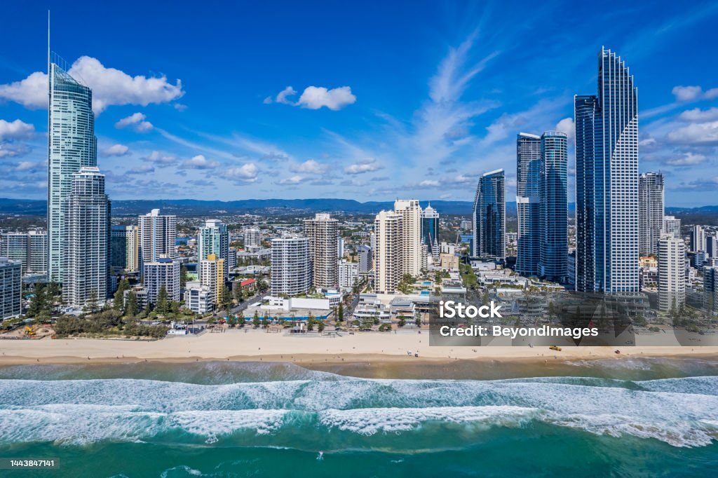 Aerial view Surfers Paradise foreshore & skyline from Pacific Ocean Aerial front view Surfers Paradise foreshore high-rise buildings from above Pacific Ocean; breaking waves in foreground, low-rise suburbs and hinterland hills on the distant horizon:higher elevation. Sunny day with some clouds. Gold Coast - Queensland Stock Photo
