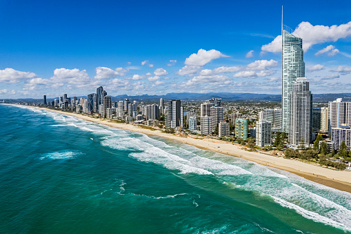 Aerial view Surfers Paradise foreshore & skyline from Pacific Ocean looking south to Broadbeach: lower elevation, warm processing. In right of frame is Q1, Australia's tallest residential tower. In background is the Gold Coast urban sprawl and Hinterland. Breaking waves & sandy beach in foreground.