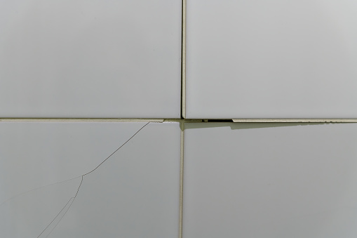 Cracked, broken bathroom wall tiles or panels - closeup view.