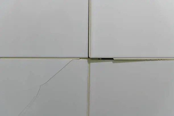 Photo of Cracked, broken bathroom wall tiles or panels - closeup view.