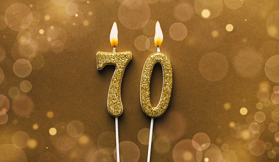 Burning golden glitter number 70 celebration candle on brown bokeh background