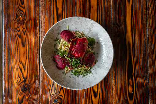 A directly above shot of a plate of bream fish with tagliatelle, shaved beetroot and parsley on a wooden table at a restaurant in Northumberland, England.