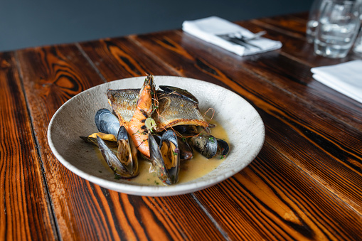 A close up shot of a plate of bream, prawns and mussels on a wooden table at a restaurant in Northumberland, England.