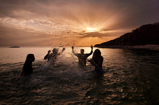 Carefree friends having fun while splashing each other during summer sunset in the sea. Copy space.