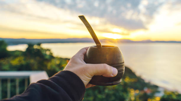 holding a mate cup with beach and mountains background at sunrise stock photo