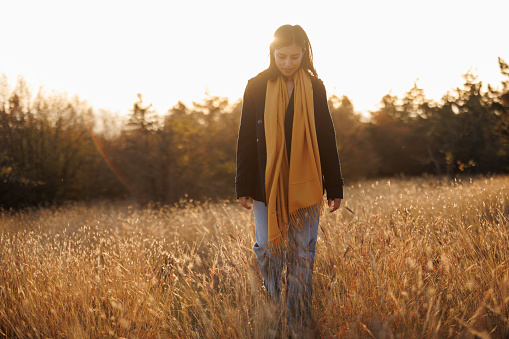 Beautiful young woman enjoying relaxing walk in autumn meadow at sunset