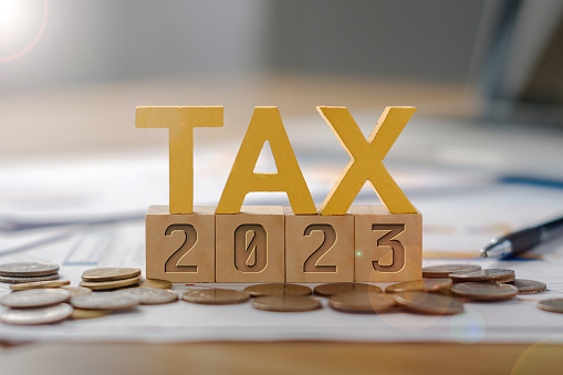 The word TAX is on a wooden block, 2023 is below. Income tax payment concept.  Return of personal income tax payable to the government  Calculation of tax returns in the years 2022 to 2023, etc.