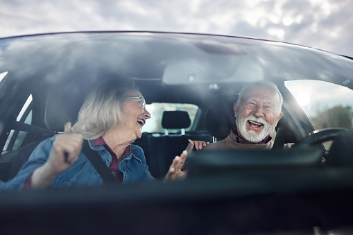 Cheerful mature couple having fun while traveling by car. The view is through glass.
