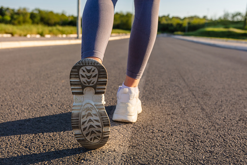 Woman running outdoors on the evening sunset. Concept of healthy lifestyle. Close up of sole of sneakers of unrecognizable athlete jogging on the road.