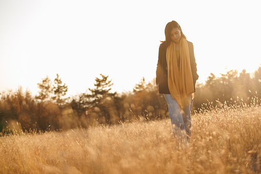 Beautiful young woman enjoying relaxing walk in autumn meadow at sunset