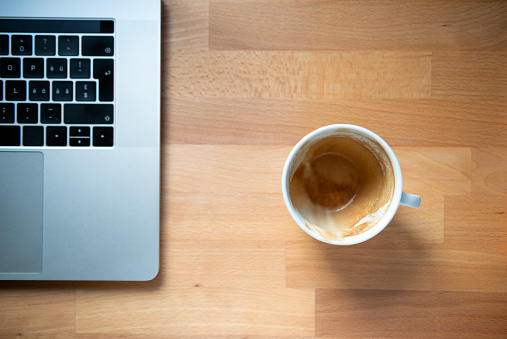 Above view of a empty cup of coffee and a laptop computer on the office, home office or cafe table for modern remote working place or technology business concepts
