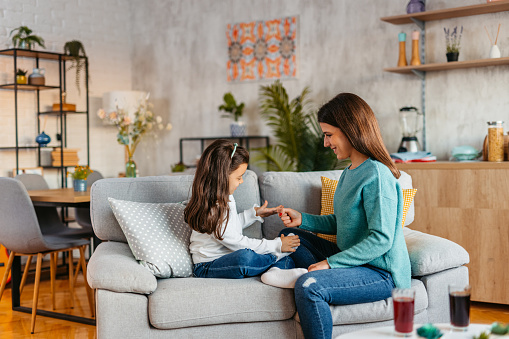 Young mother and her daughter playing together on the sofa in the living room. Playing rock, paper, scissors.