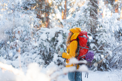 Female hiker in winter forest with backpack enjoys the magic of snowfall and winter forest. Mental health and peace during secluded walks in nature.