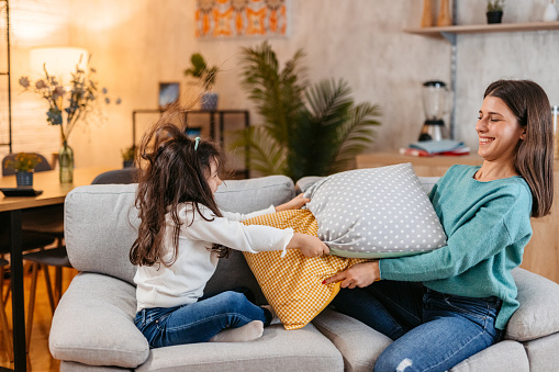 Young mother and her daughter having a pillow fight on the sofa in the living room.
