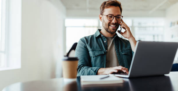 software designer speaking to his client on the phone in an office - men laptop businessman using laptop imagens e fotografias de stock