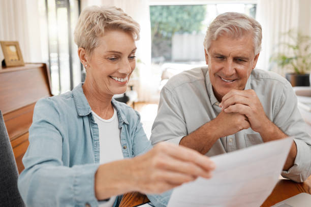 istock Happy couple, reading and paperwork or document for bill, mortgage or retirement plan or payout while sitting at home. Mature man and woman busy with tax compliance or finance form for pensioners 1443879056