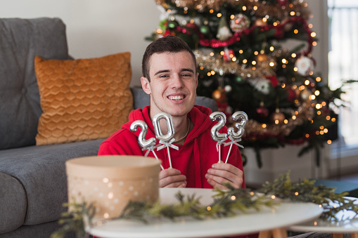 Happy teenage boy sitting at home with balloons shaped as numbers when celebrating New Year