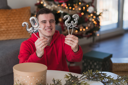 Cheerful boy sitting at home during winter holidays and playing with balloons shaped as a number 2023