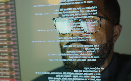 Stock photograph of an afro Caribbean (afro American) man studying a see through display depicting Python computer coding.