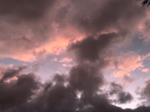 Horizontal cloudscape with pink and dark grey cumulus clouds against a blue sky at sunset. New England high country, NSW