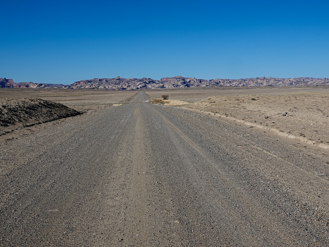Remote gravel road disappearing into the distance against the rocky escarpment of the San Rafael Reef.