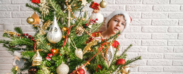 little child with decorated christmas tree, copy space. - christmas child little boys peeking imagens e fotografias de stock