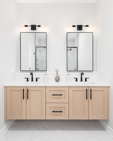 A modern bathroom with a wooden vanity cabinet, black faucets, white marble countertop, and black rimmed square mirrors.