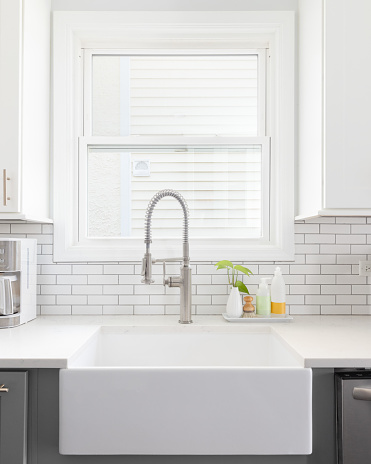 A kitchen sink detail shot with white and grey cabinets, a farmhouse sink, and white subway tile backsplash.