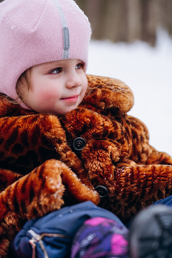 portrait of a little girl in a fur coat and a knitted pink hat in a snowy winter park