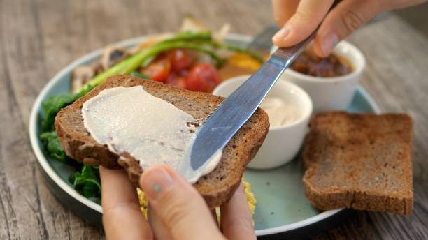 breakfast in the fresh air in your favorite cafe. a plate with vegetables and tofu for a complete diet. close-up of a knife spreading sauce on a piece of whole grain toast. - butter toast bread breakfast imagens e fotografias de stock