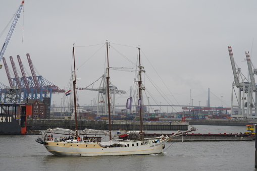 Hamburg, Germany, 08 27 2022, Passenger sailing ship under the flag of Netherlands MARE FRISIUM  is sailing through Hamburg port during overcast and rainy weather. Behind are container terminals.