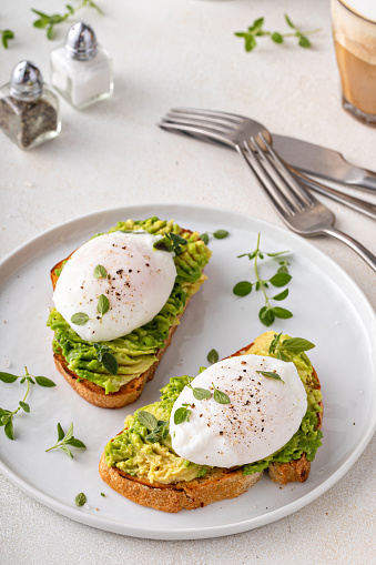 Avocado toast with a perfect poached egg on top with salt and pepper served with coffee for breakfast