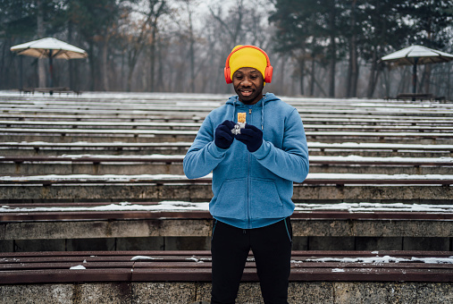 Young cheerful sporty man eating snack during running pause on cold winter day