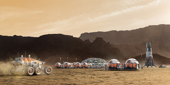 Martian base camp, with a rover moving in the foreground with dust towards a base camp made from linked geometric units with solar panels and a greenhouse with plants, and a docked rocket and Mars rover in the background. The camp is close to dark mountains under a bright sky.