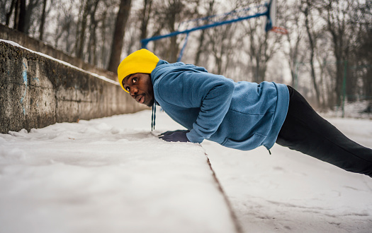 Young sporty African man doing push-ups in the snow