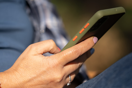 Closeup of female hands using a smart phone, nature background.