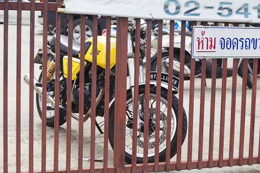Yellow colored motorcycle Centaur behind gate parked in residential district of Bangkok Chatuchak