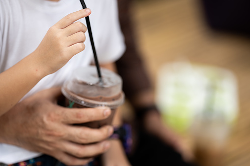 Chocolate milk is being held and drunk by a girl that wearing white shirt.