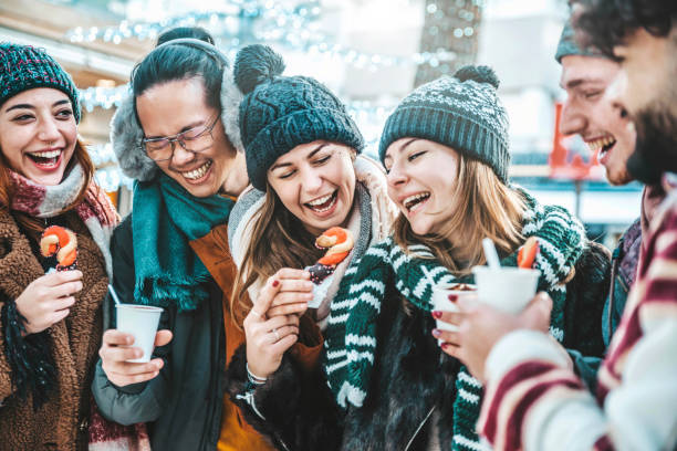 glückliche freunde, die spaß haben, glühwein und heiße schokolade auf dem weihnachtsmarkt zu trinken - fröhliche junge leute, die winterferien am wochenende genießen - fokus auf asiatischen kerl - people eating walking fun stock-fotos und bilder