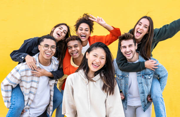 Diverse community of young people smiling together on a yellow wall background - Multiracial college students having fun laughing outside - Youth culture concept stock photo