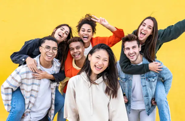 Diverse community of young people smiling together on a yellow wall background - Multiracial college students having fun laughing outside - Youth culture concept