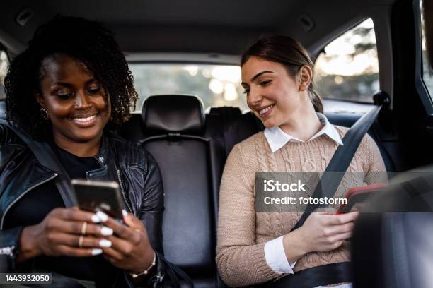 Two Young Women Riding In The Back Seat Of A Taxi Using Their Smart Phones To Pass The Time Stock Photo - Download Image Now