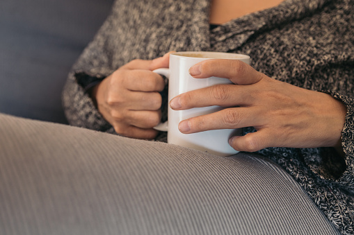 mature woman's hands holding a mug of hot latte in the morning. coffee time at dawn.